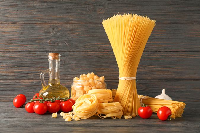 Composition with pasta, olive oil, tomatoes and garlic on wooden table, space for text