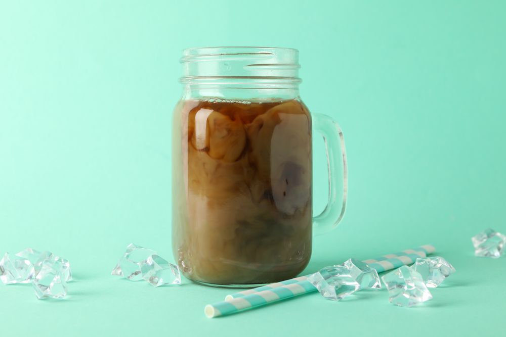 Jar of ice coffee, ice cubes and straws on mint background