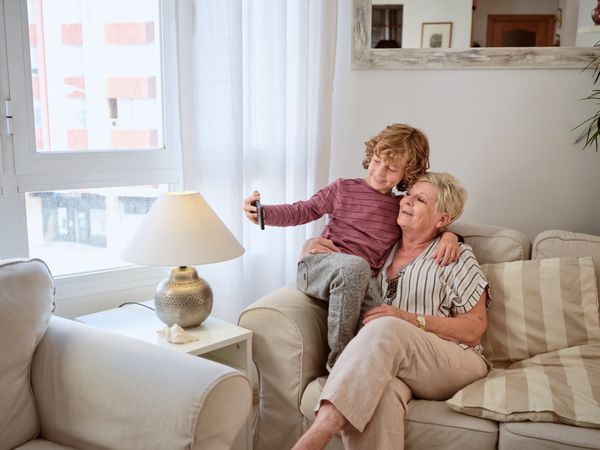 Older woman on sofa with grandson using smartphone together