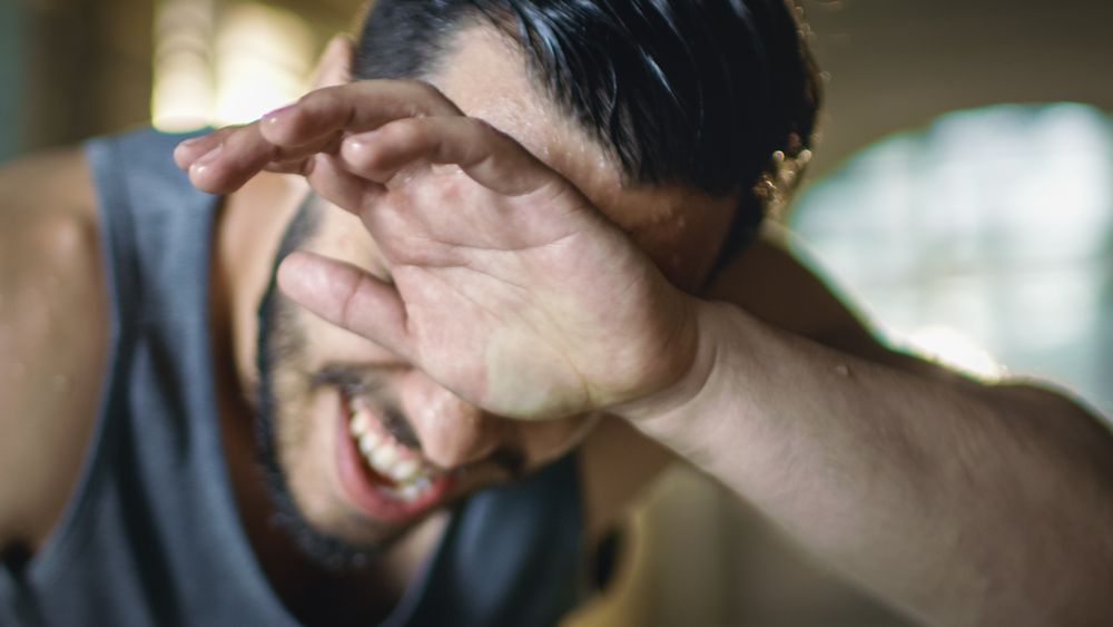 Close-up Shot of Exhausted Bend Muscular Man Wipes His Forehead with a Hands and Rests After Intensive Workout.