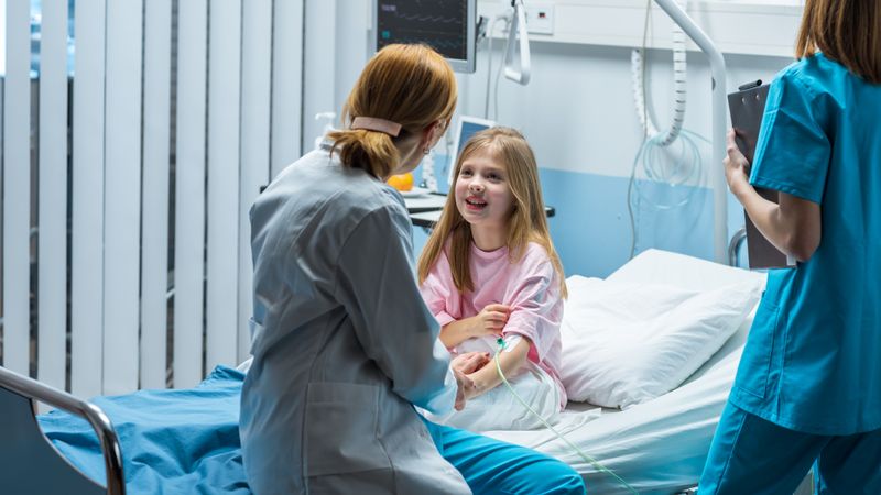 Cute Little Girl Sits on a Hospital Bed and Talks with Friendly Woman Doctor Taking Blood Test