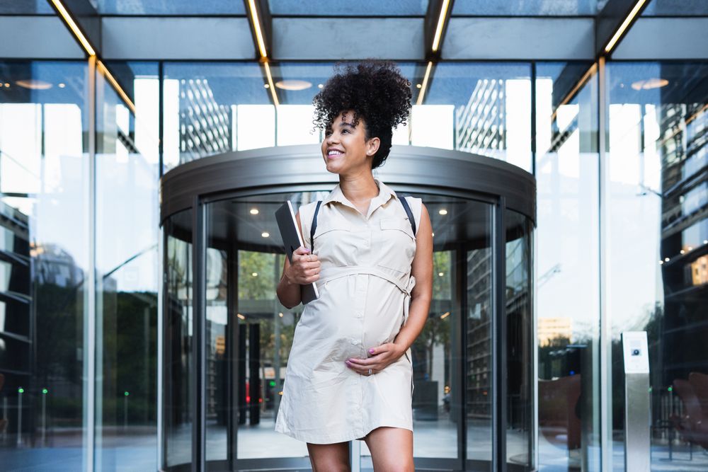 Smiling Black woman with laptop coming out of office building