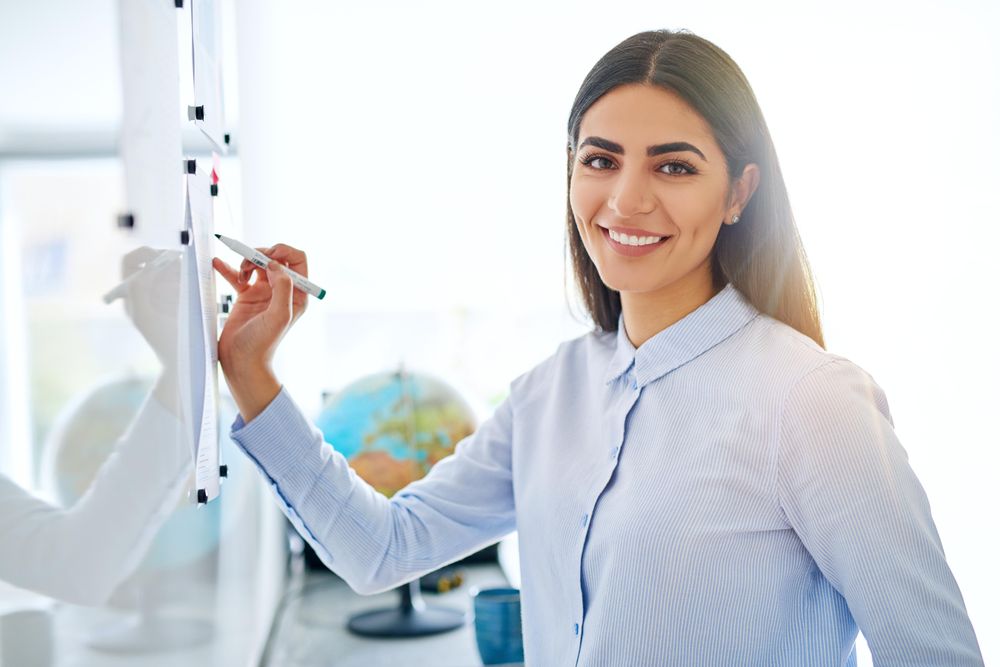 Happy Arab female working through problem on dry erase board