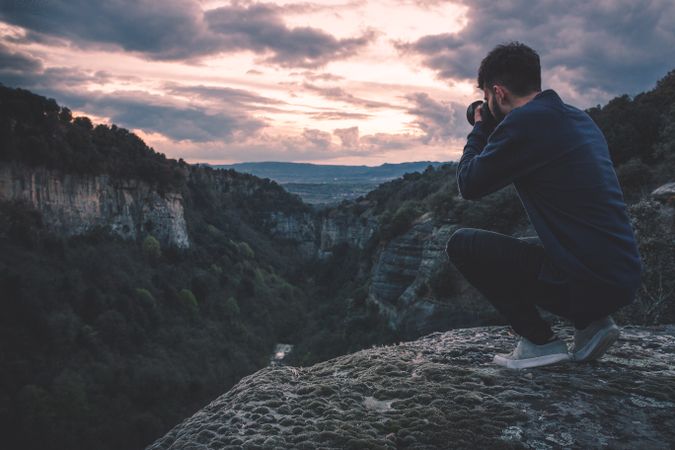 man with photo camera sitting on hill mountain with magnificent sunset