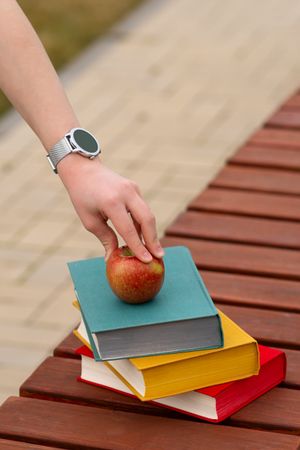 Red apple atop colorful hardcover books held by person's hand.