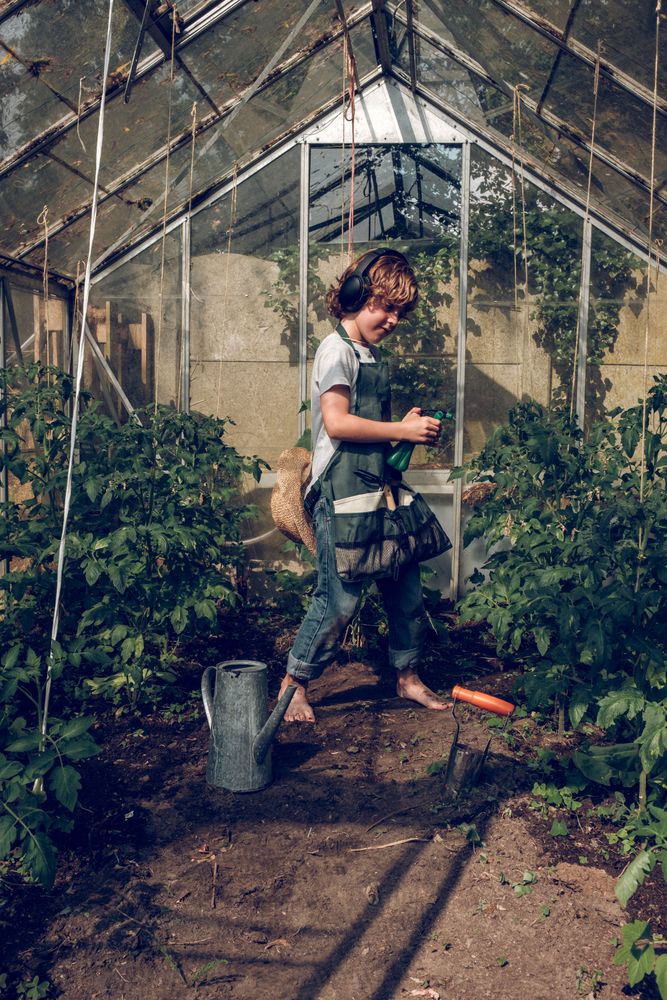 Cheerful boy in headphones working in greenhouse