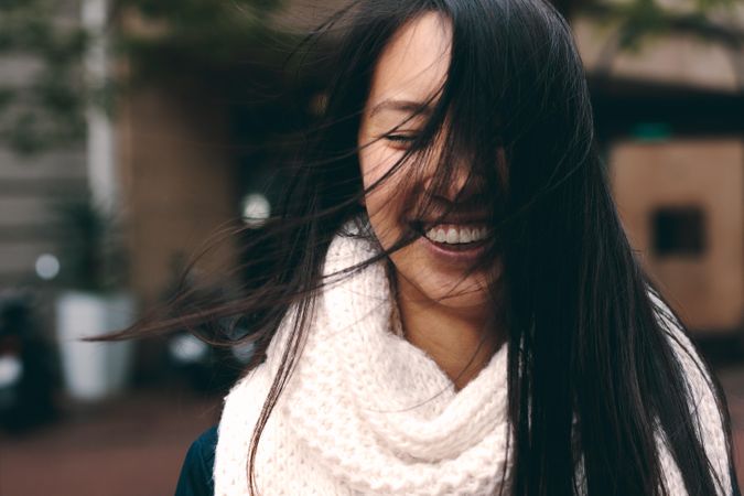 Smiling Asian woman with windswept hair covering face