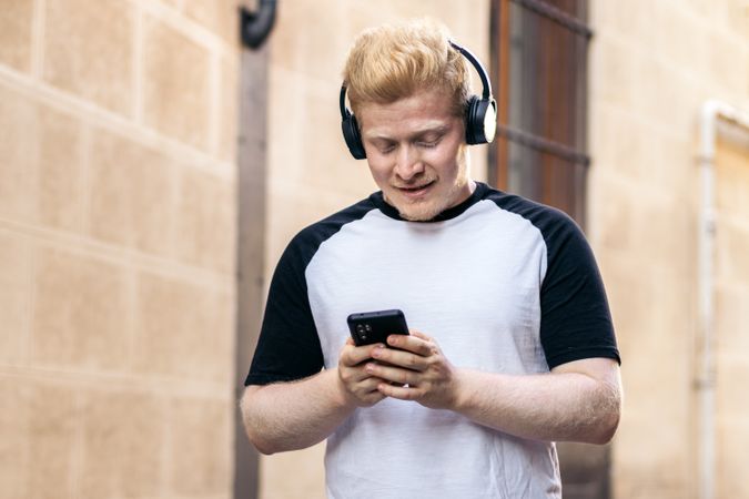 Latino man with albinism walking down the street using smartphone and listening to music with headphones