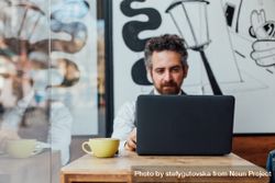 Man sits in window of cafe with laptop 0yaOa0
