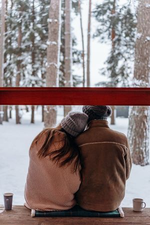 Back view of man and woman sitting on bench in snow covered woods
