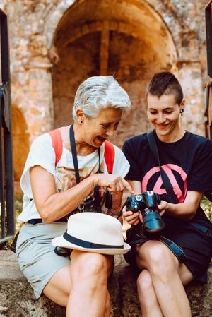 Stylish young woman showing photography to mature woman on stony steps