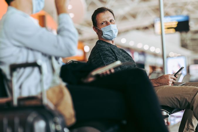 Man in face mask glancing back while waiting for delayed flight