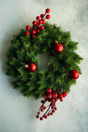 Christmas wreath with red baubles and holly on marble counter, vertical composition