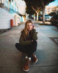 Woman in green jacket sitting on sidewalk