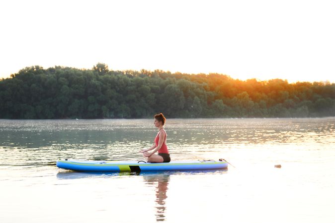 Side view of woman peacefully meditating on paddleboard