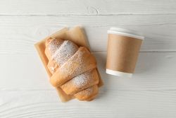 Flat lay of take away from cafe of croissant and cup of coffee on plain background