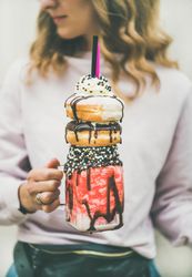 Woman holding stacked donut milkshake with straws, whipped cream, and chocolate sprinkles