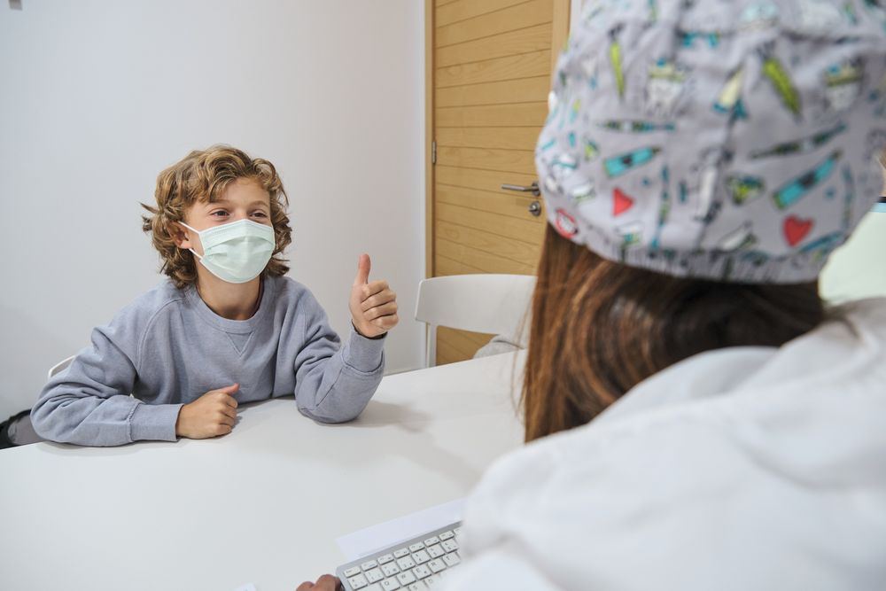 Boy showing approval gesture to doctor at table
