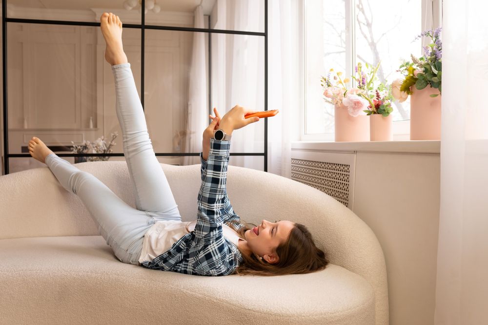 Joyful teen girl lying comfortably taking selfies at home.