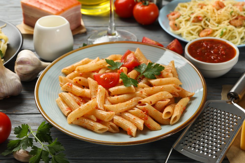 Composition with plate of tasty pasta and ingredients for cooking on wooden background