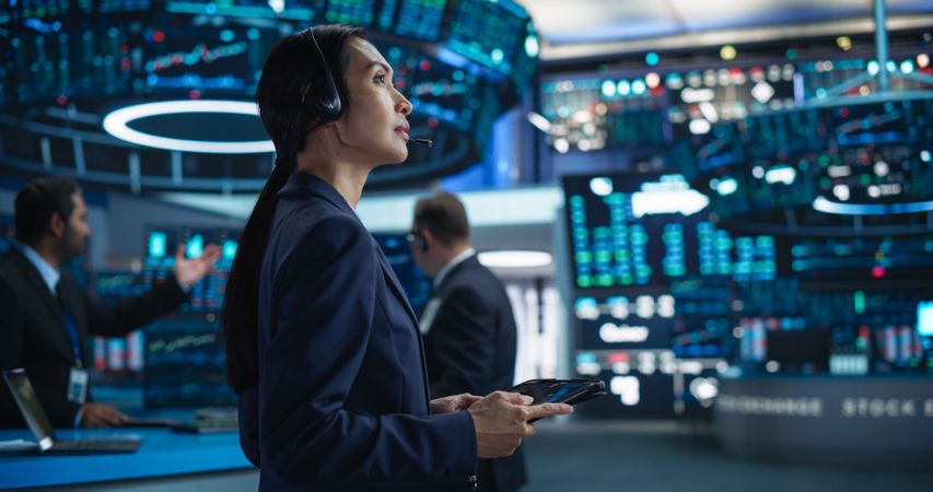 Female Investment Banker Wearing Headphones and Using a Tablet Computer with Financial Market Analytics Data.