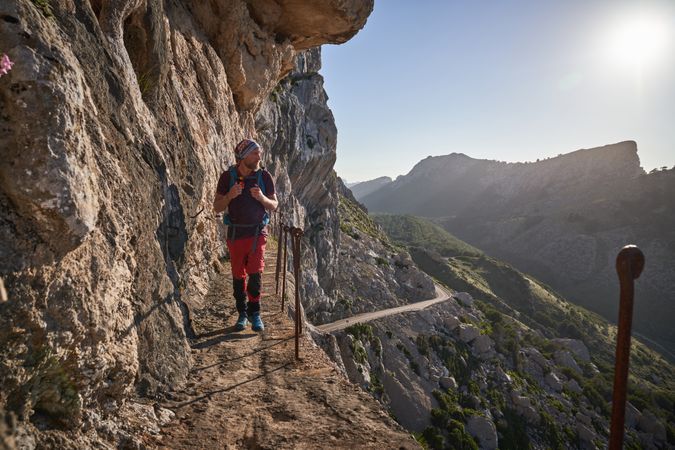 Male hiker with backpack walking on path on cliff