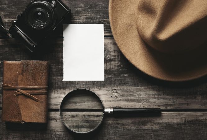 Hat, note book, camera, paper and magnifying glass on table