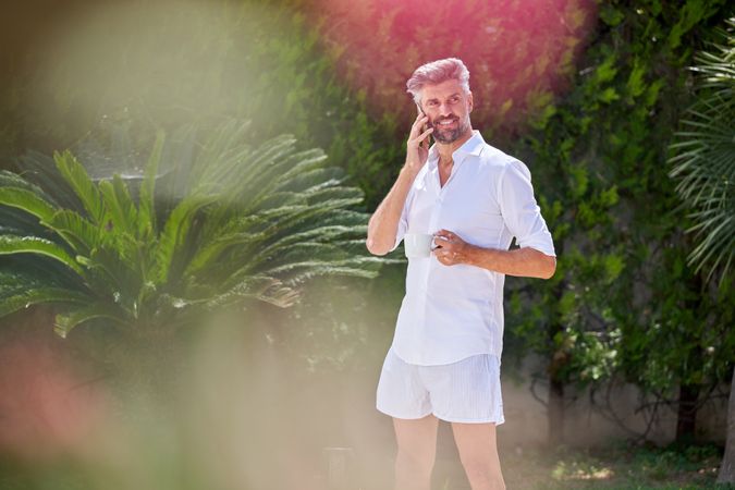 Positive man talking on mobile phone in tropical garden