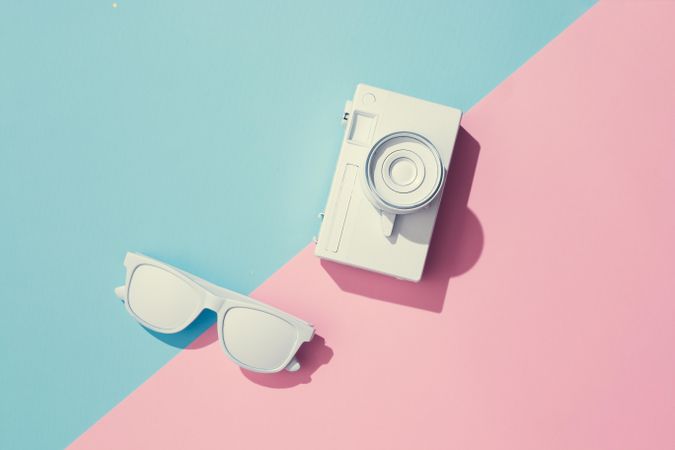Painted sunglasses and camera with pastel pink and blue background