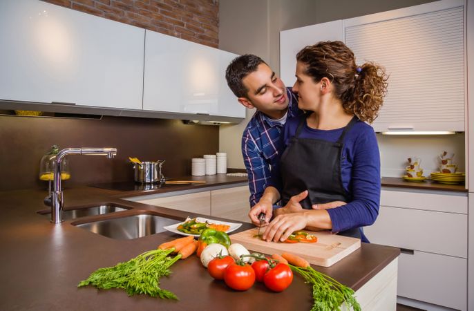 Loving couple in kitchen together as woman chops vegetables in kitchen with space for text