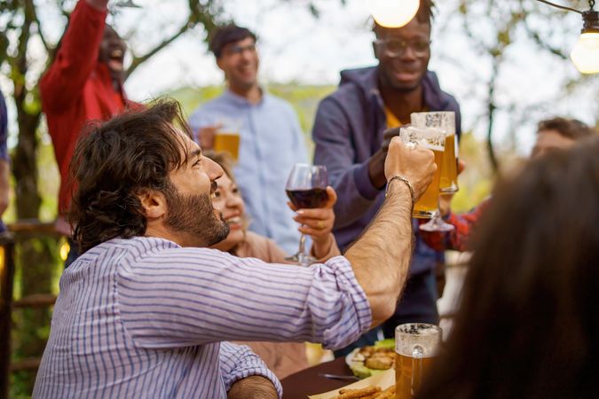 A cheerful group of multi-ethnic friends toasting with wine and beer at an outdoor party