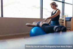 Woman lying with her back on a fitness ball doing pilates training bxLZjb