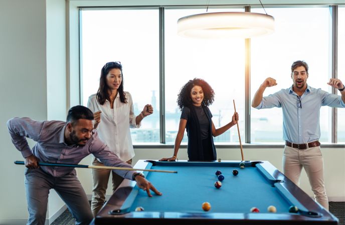 Young men and women playing billiards at office after work