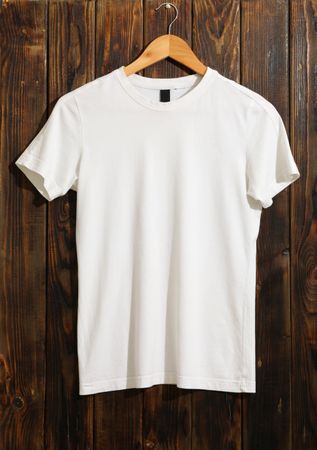 Hanger with blank plain t-shirt on wooden background, space for text