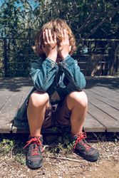 Upset boy sitting on wooden boardwalk and covering face