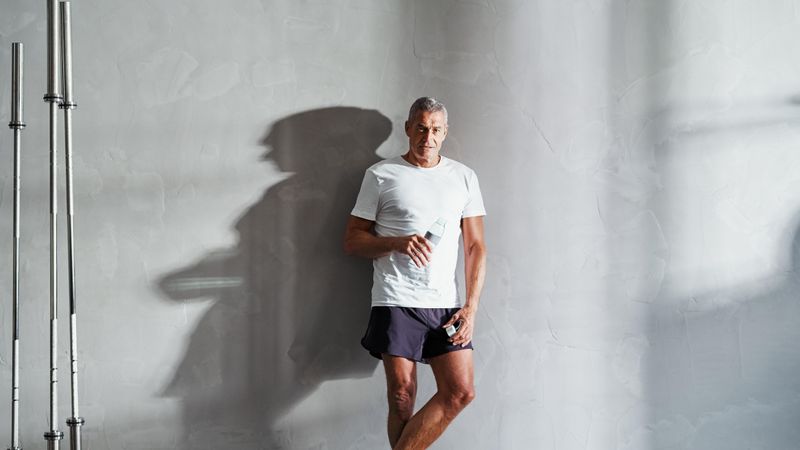Man standing against the wall with water after exercising with water bottle