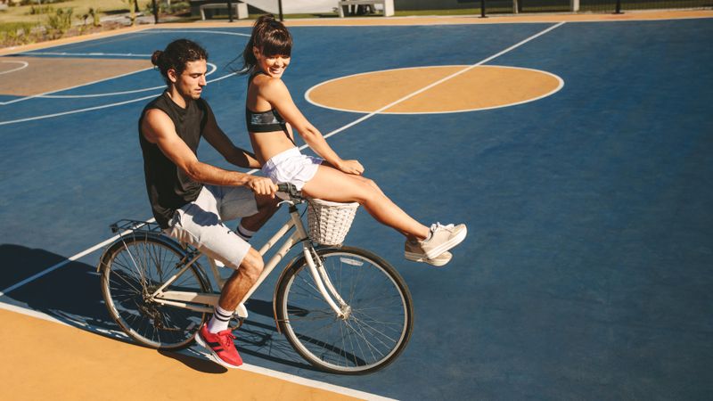 Young man riding bicycle with woman sitting on handlebar