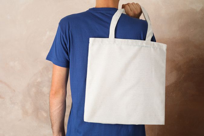 Young man holding tote bag against brown background, empty space