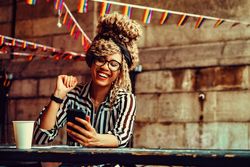 Laughing Black woman in stripe shirt texting on phone in cafe