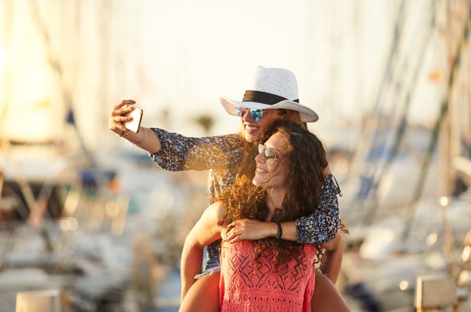 Woman carrying girlfriend on back and taking selfie