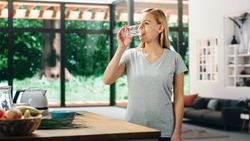 Young Adult Woman with Blond Hair Wearing Gray V-Neck T-Shirt, Drinking a Glass of Water After Lunch.