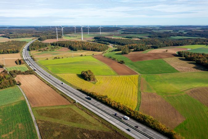 Drone shot with curved highway and wind turbines at the horizon in an autumn scenery