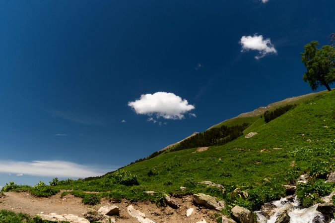 Single cloud above green hillside with blue sky.