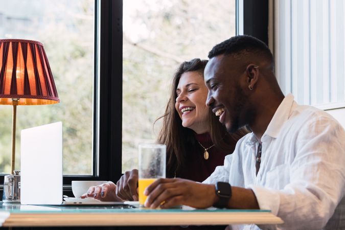 Cheerful multiethnic couple using laptop during breakfast at home