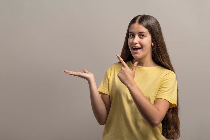 Excited young woman pointing to her empty palm, presenting a product.