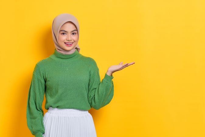 Smiling woman in headscarf with her palm up towards copy space