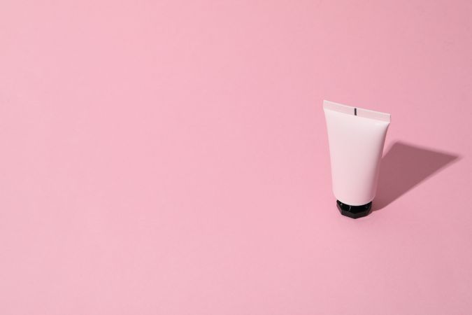 Tube of cosmetic on pink background, space for text