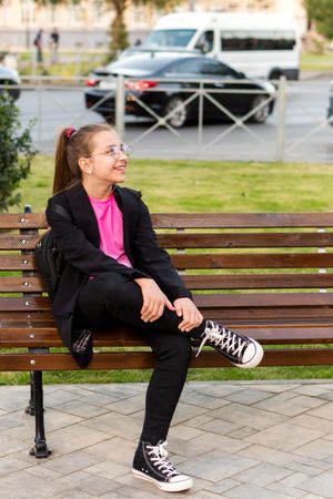 Girl sitting casually on bench and looking around.