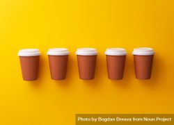 Single row of disposable coffee cups on yellow background beq1Pb