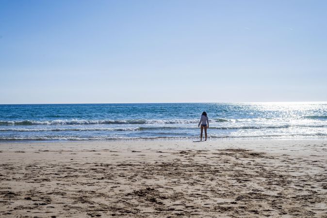 Woman in distance standing on the same as the waves come in